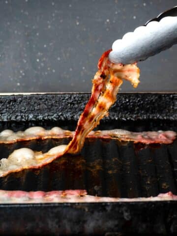 Crispy bacon in grill pan with tongs.