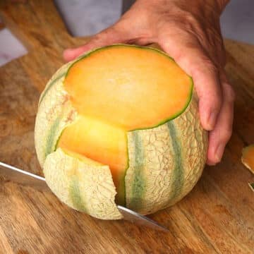 Cantaloupe on cutting board with knife.