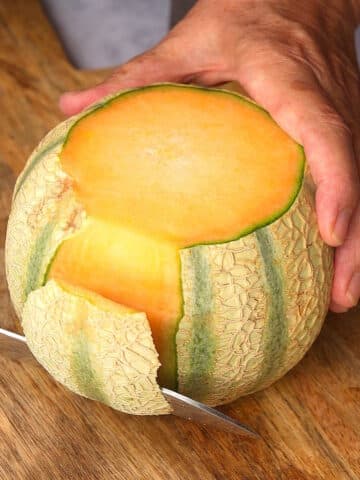 Cantaloupe on cutting board with knife.