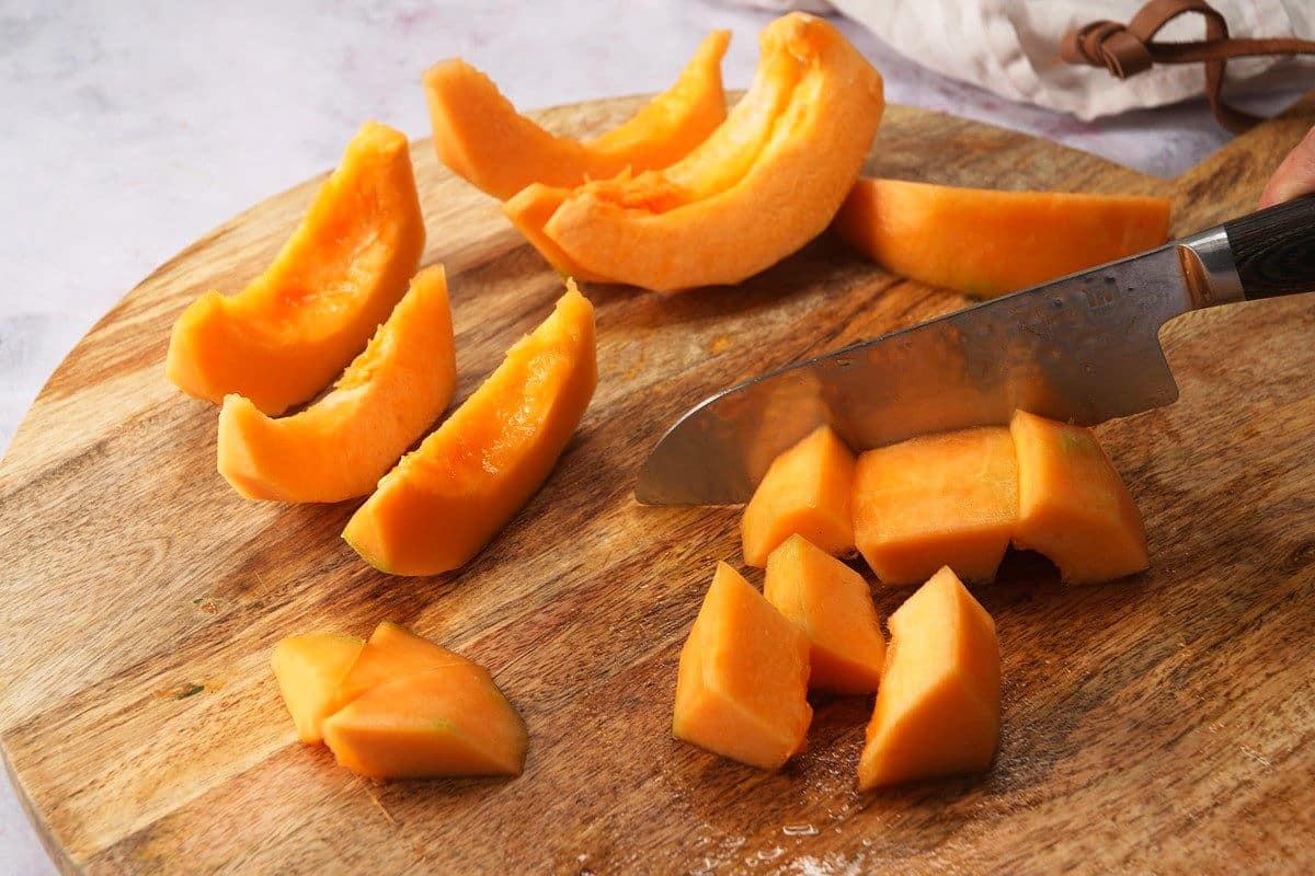 Cantaloupe wedges and cubes on cutting board with knife.