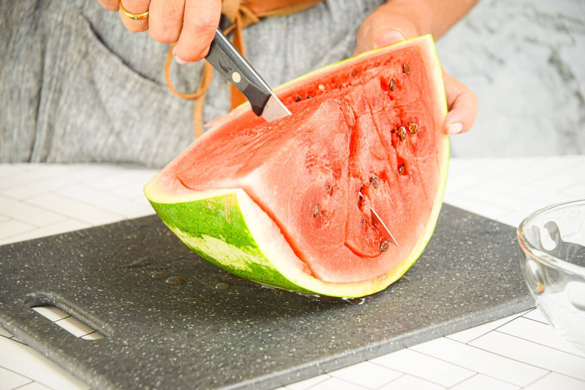 Woman making cuts into watermelon quarter.