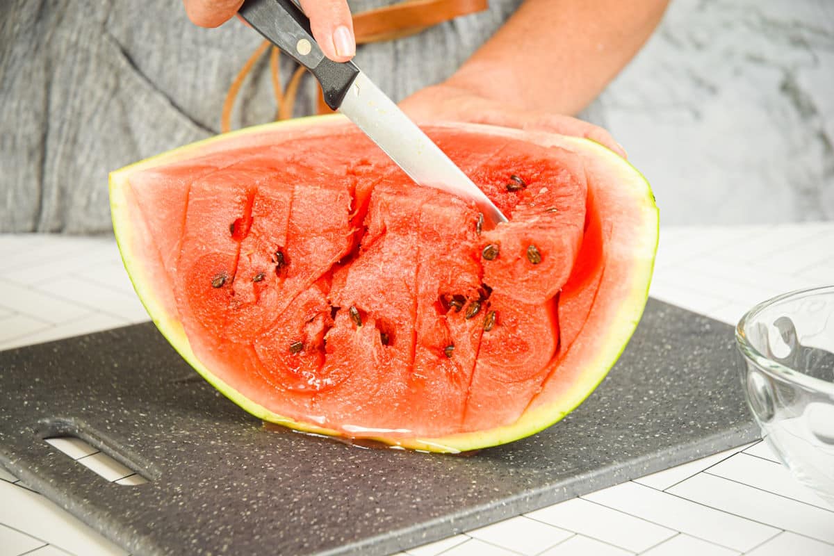 Woman slicing watermelon quarter vertically.