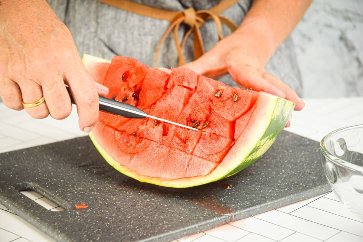 Woman cutting watermelon into cubes.