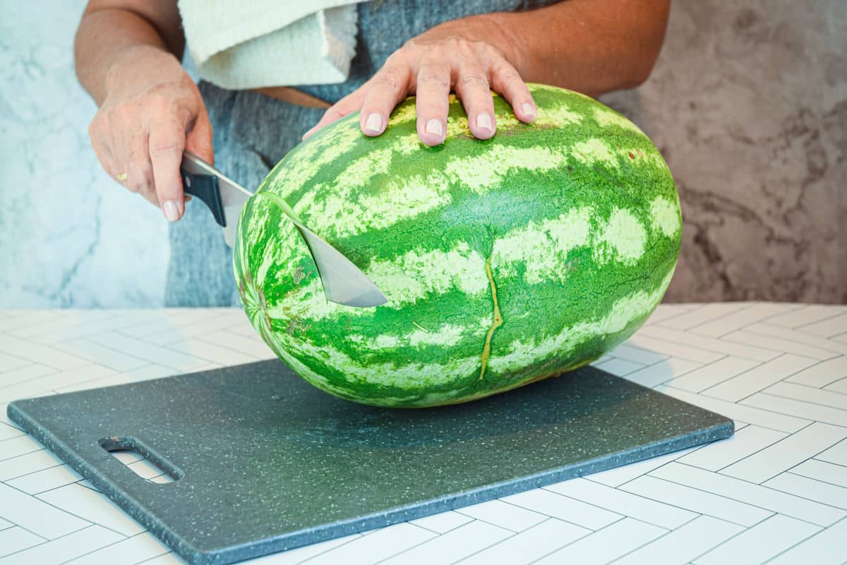 Woman slicing ends off of large watermelon.