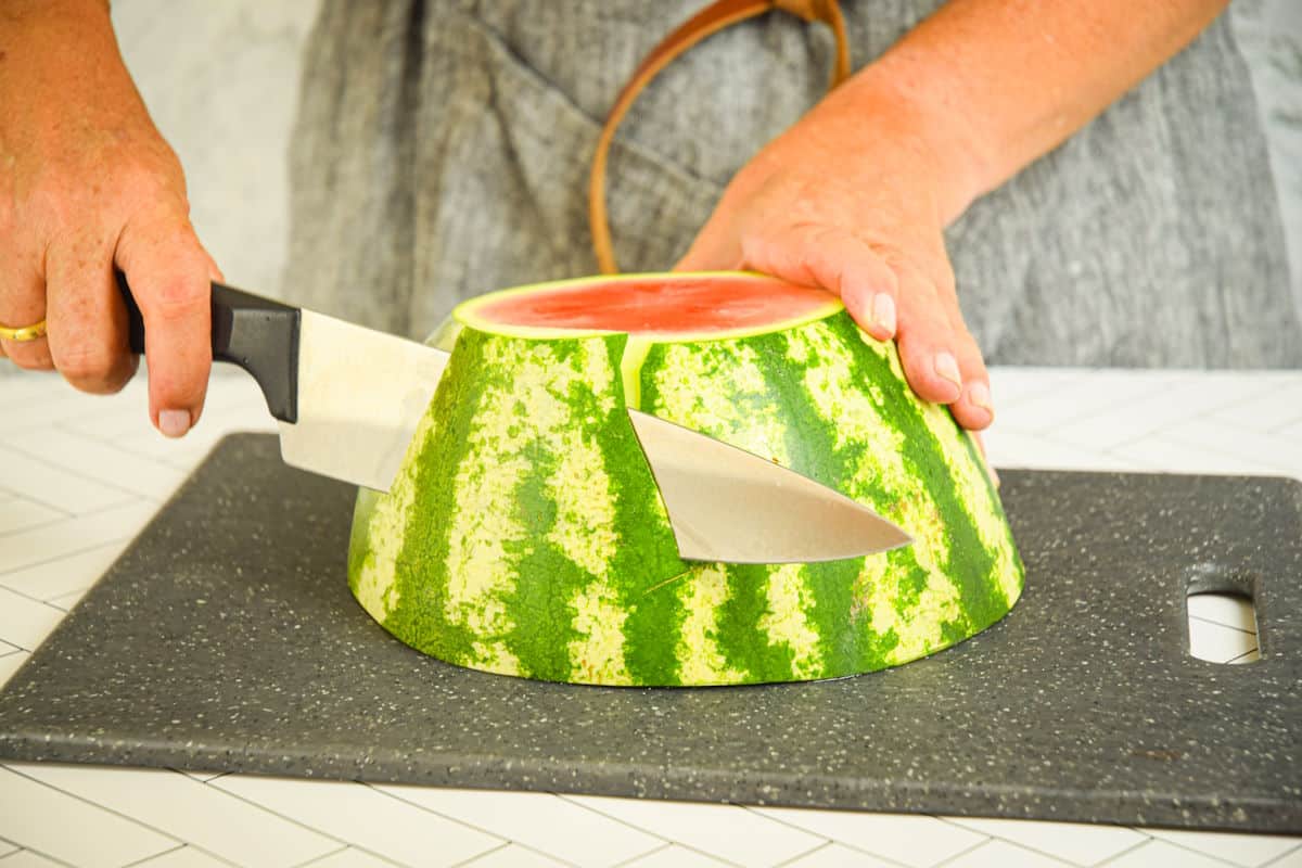 Woman peeling watermelon with chef's knife.