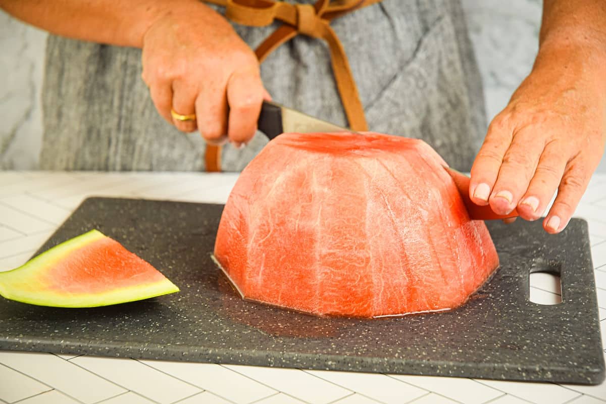 Woman making vertical cuts into peeled watermelon.