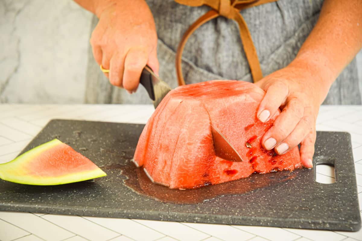 Woman cutting peeled watermelon into sticks.