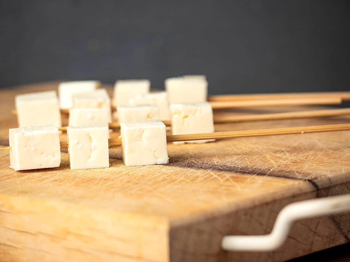 Skewered tofu cubes on cutting board.