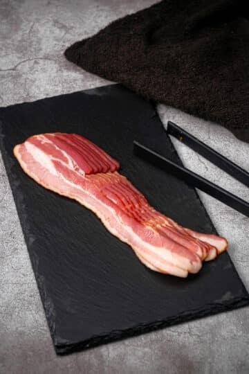 Raw bacon strips on black board.