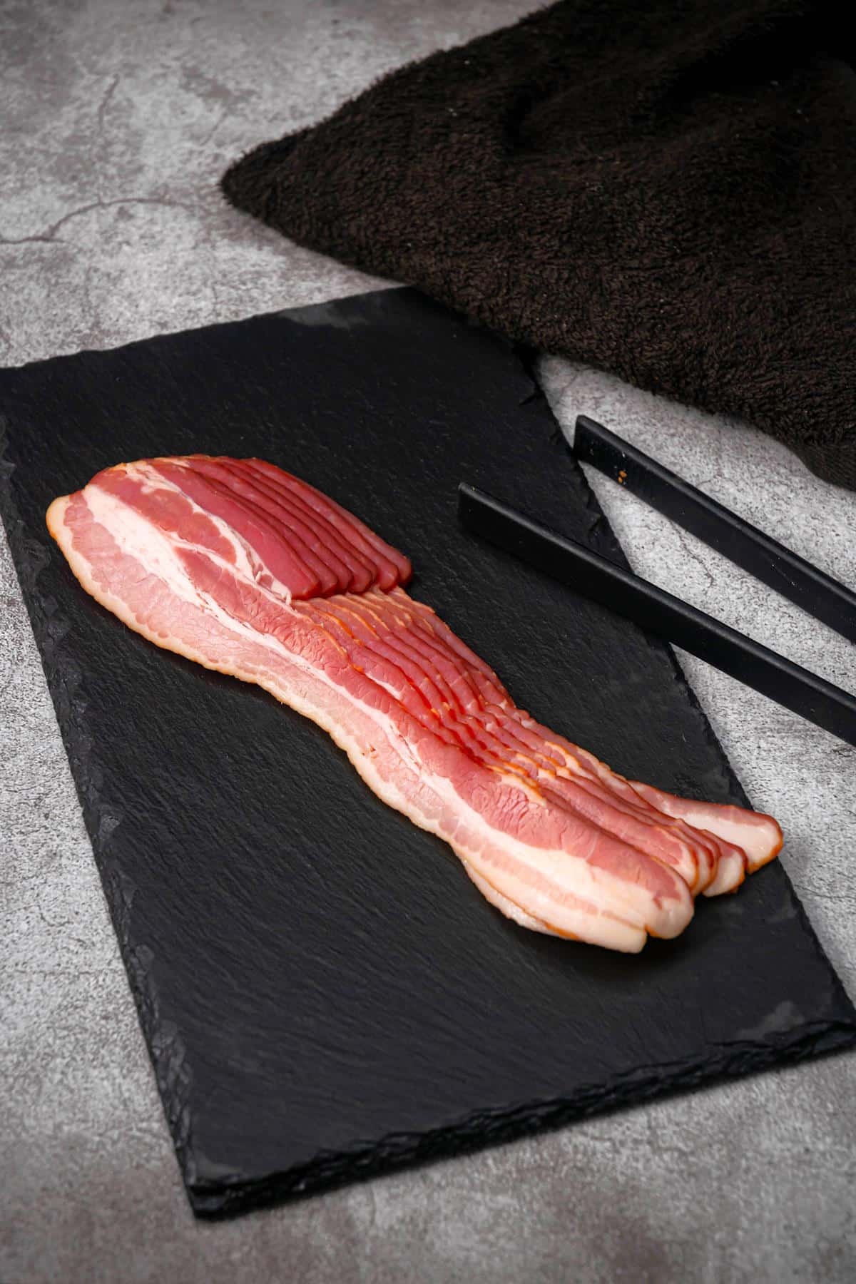 Raw bacon strips on black board.