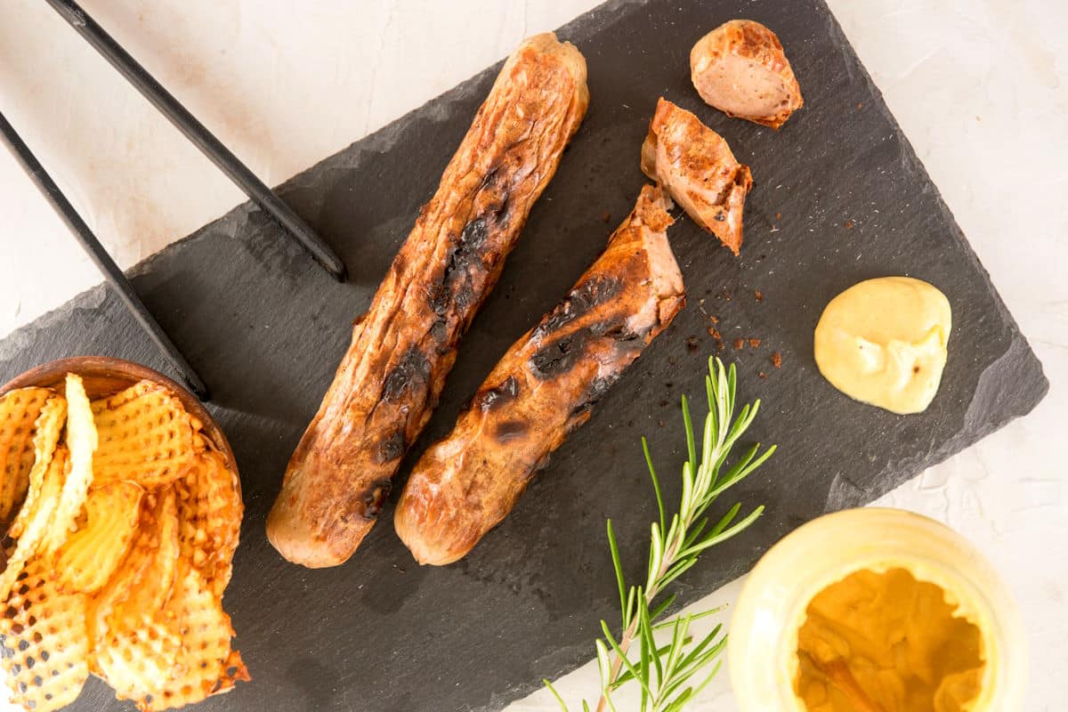 Grilled bratwurst on serving board with mustard and waffle chips.