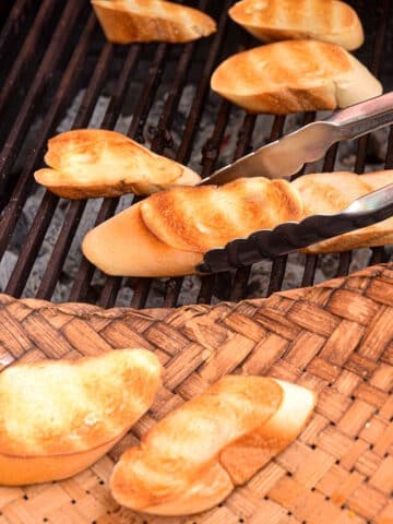 Grilled bread on outdoor grill with tongs.