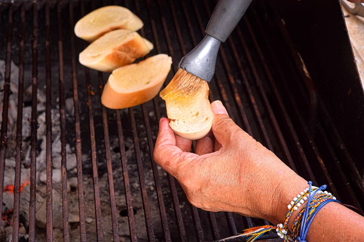Bread getting brushed with olive oil on grill.