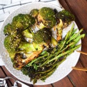 Grilled broccoli on plate with tongs.