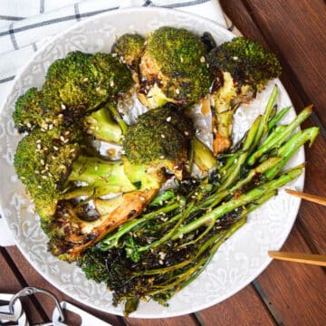 Grilled broccoli on plate with tongs.