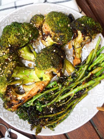 Grilled broccoli on plate with tongs.