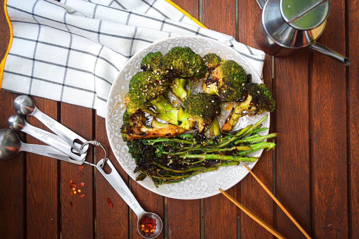 Grilled broccoli on plate on wooden table with tongs.
