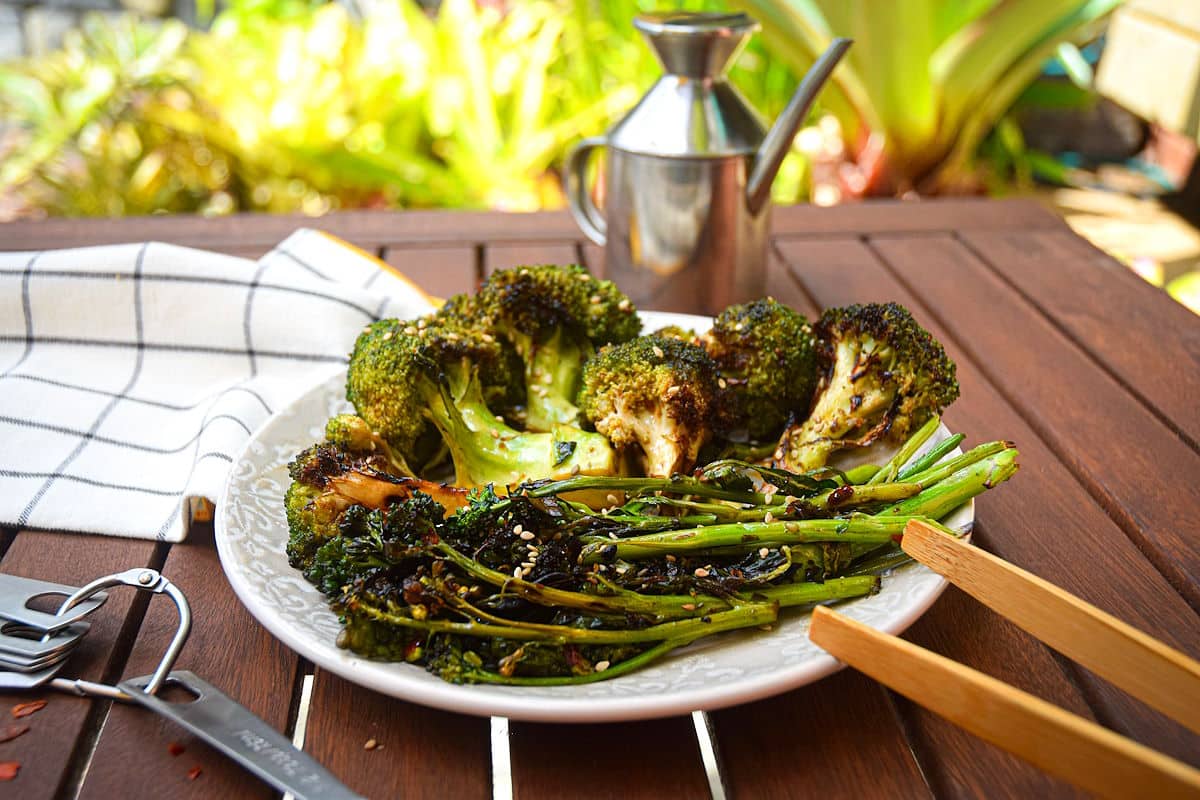 Grilled broccoli on plate on outdoor wooden table.