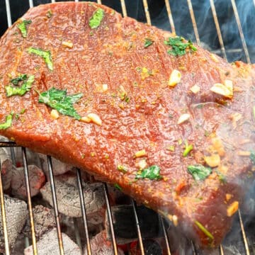 Marinated flank steak cooking on charcoal grill.