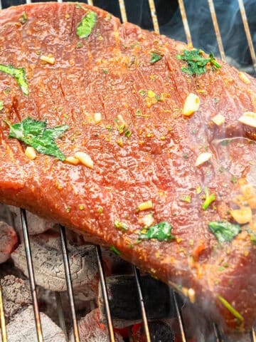 Marinated flank steak cooking on charcoal grill.