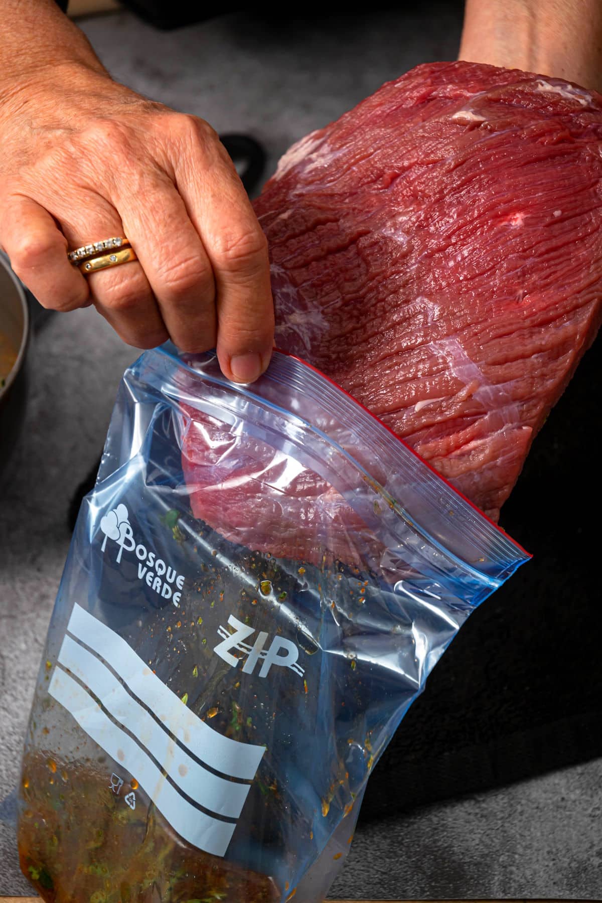 Flank steak getting transferred to bag of marinade.