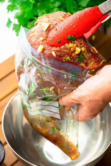 Raw, marinated flank stank in tongs.