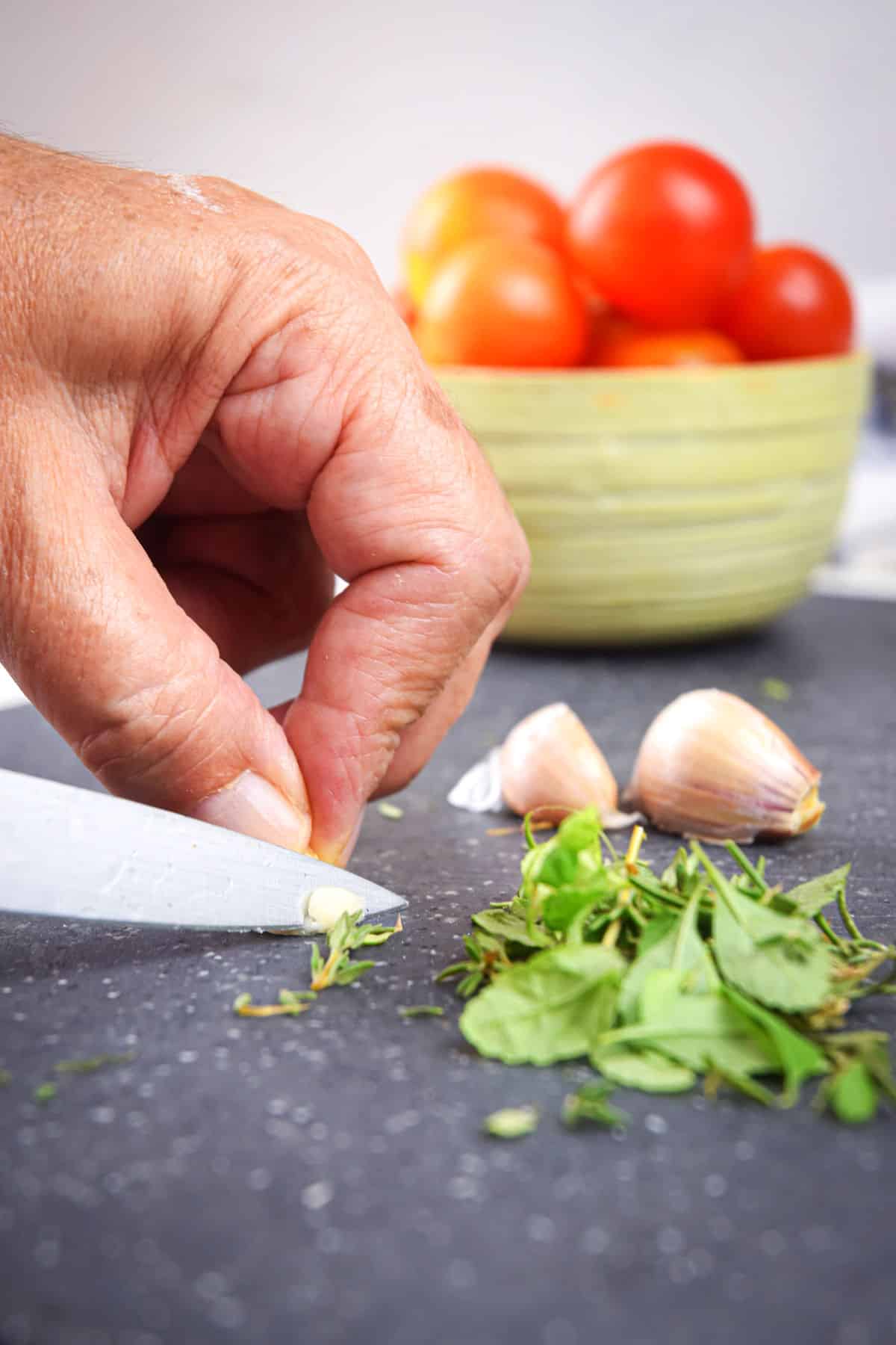 Woman's hand chopping herbs on cutting board.