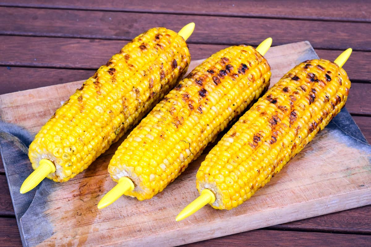Grilled corn on cutting board with corn forks.