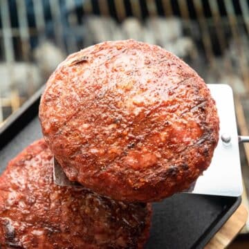 Grilled burgers on metal flipper, grill grates in the background.
