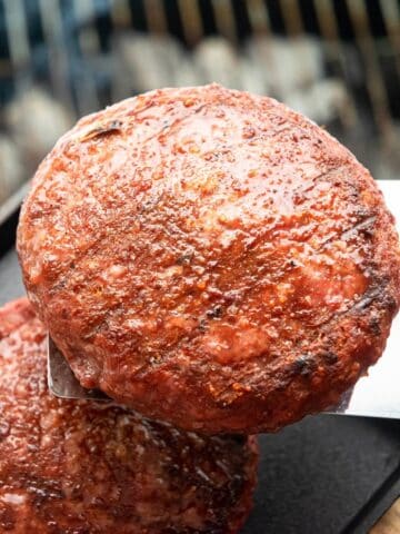 Grilled burgers on metal flipper, grill grates in the background.