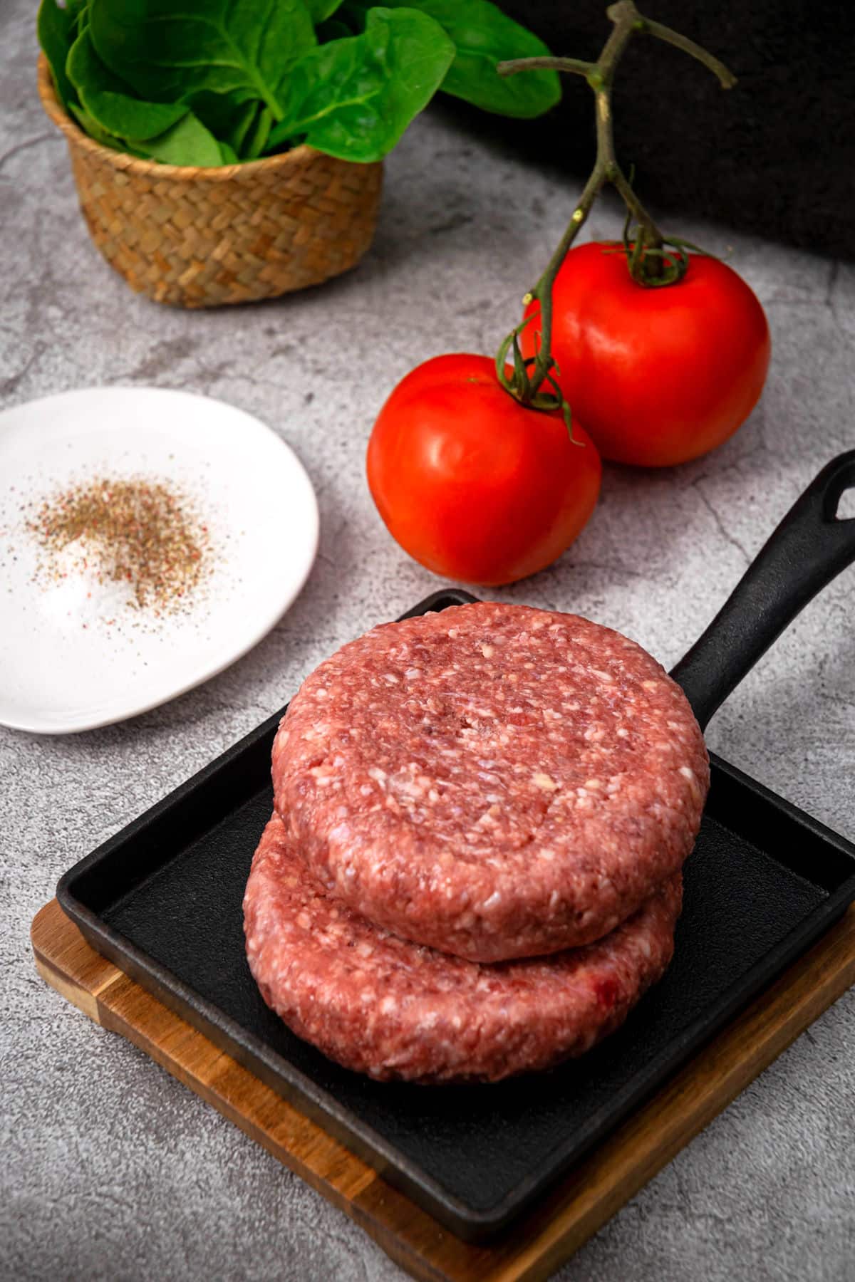 Raw frozen burger patties on cast iron dish.