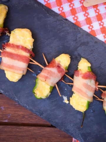 Grilled jalapeño poppers on black serving board.