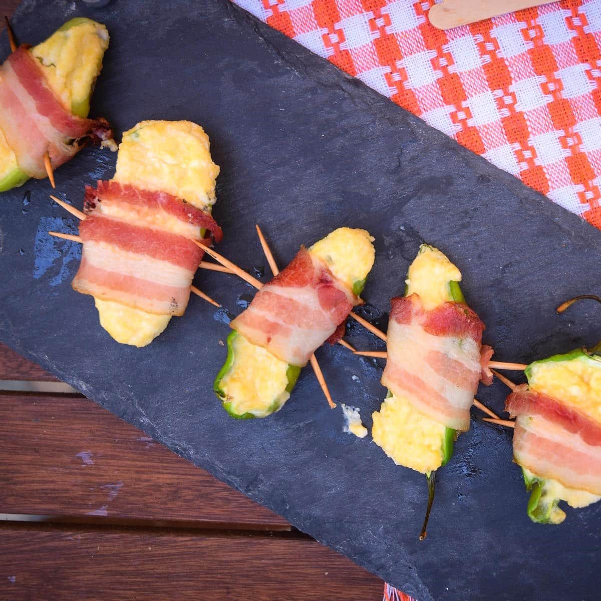Grilled jalapeño poppers on black serving board.