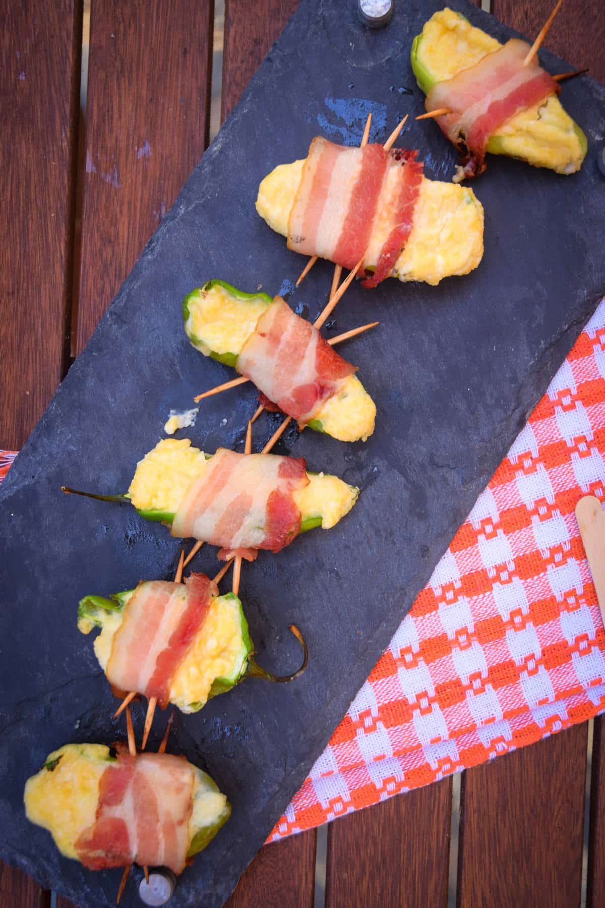 Grilled jalapeño poppers with toothpicks on black serving board.