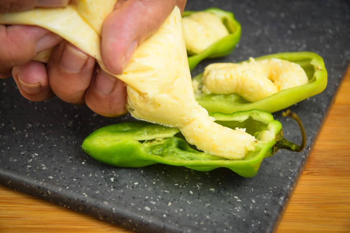 Cheese filling getting squeezed into open jalapeño pepper.