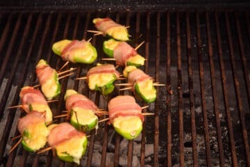 Jalapeño poppers cooking on the grill over charcoal.