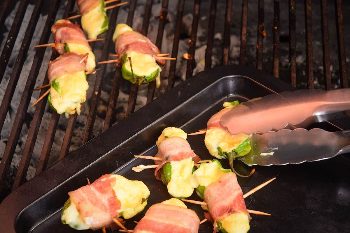 Jalapeño poppers on grill and baking sheet with tongs.