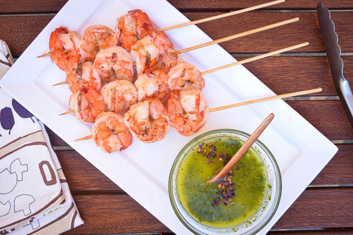 Jumbo shrimp on wooden skewers with chimichurri on the side.