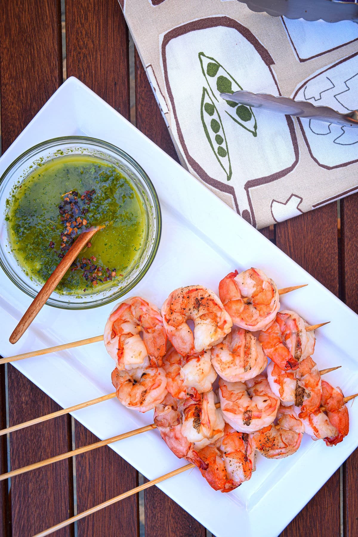 Jumbo shrimp on wooden skewers on white dish with chimichurri sauce in a bowl.