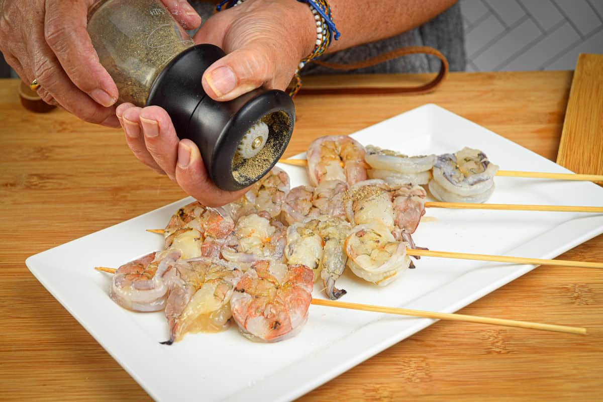 Raw jumbo shrimp skewers getting seasoned.