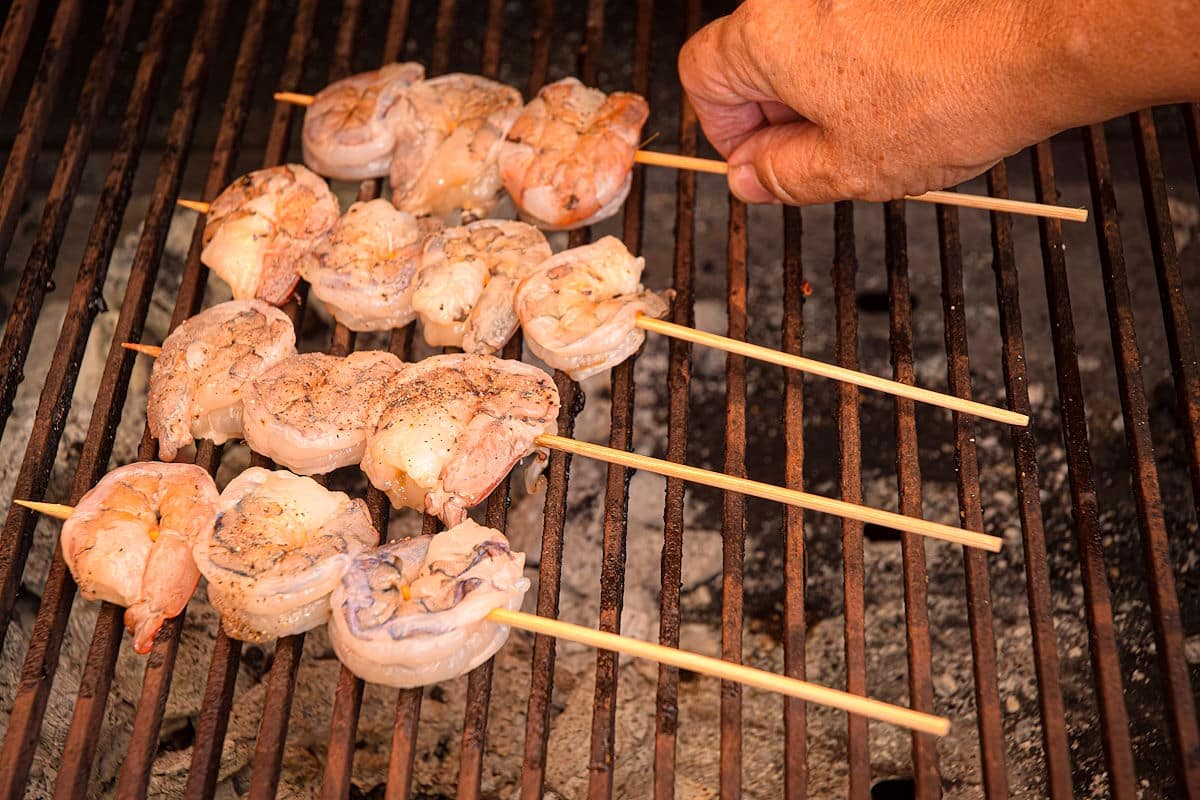 Raw jumbo shrimp skewers on charcoal grill.