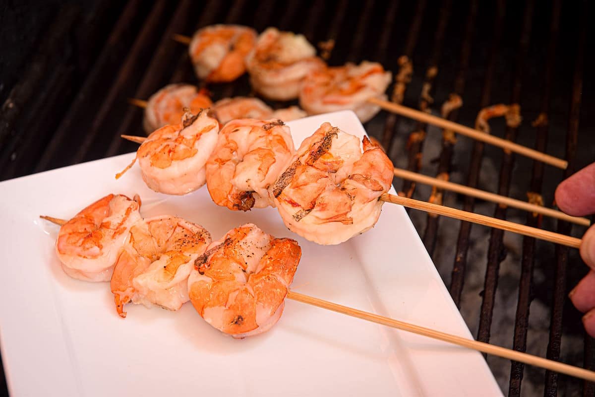 Grilled jumbo shrimp getting transferred from grill to white dish.