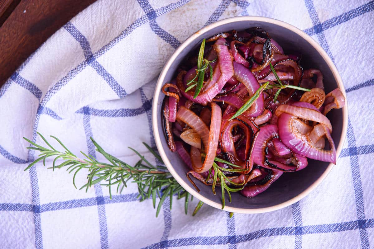 Grilled red onion rings in bowl with fresh rosemary.