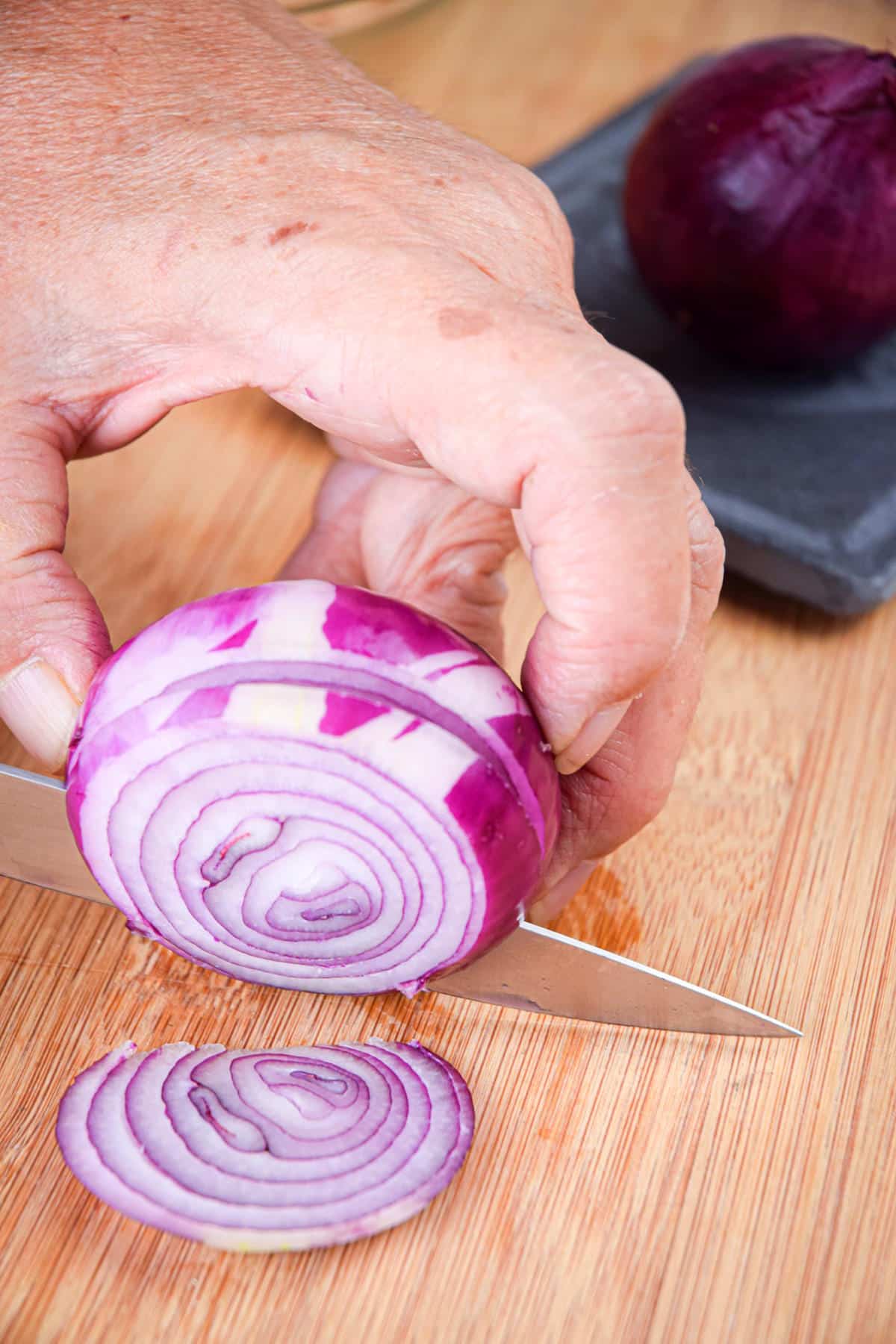 Red onion getting sliced into rings on cutting board.