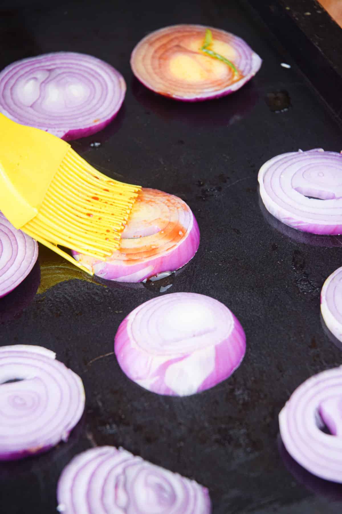 Red onion rings on grill getting brushed with vinaigrette.