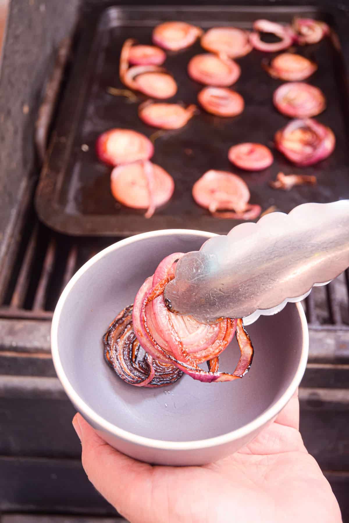 Grilled onion rings in tongs and small bowl.