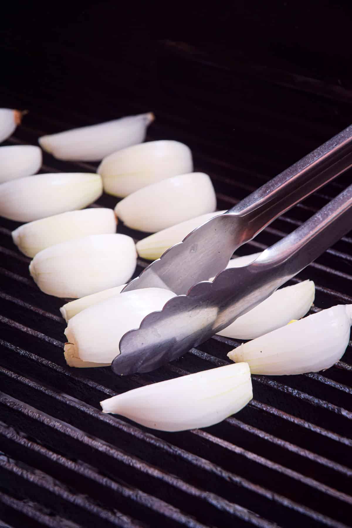 Onions wedges on grill with tongs.