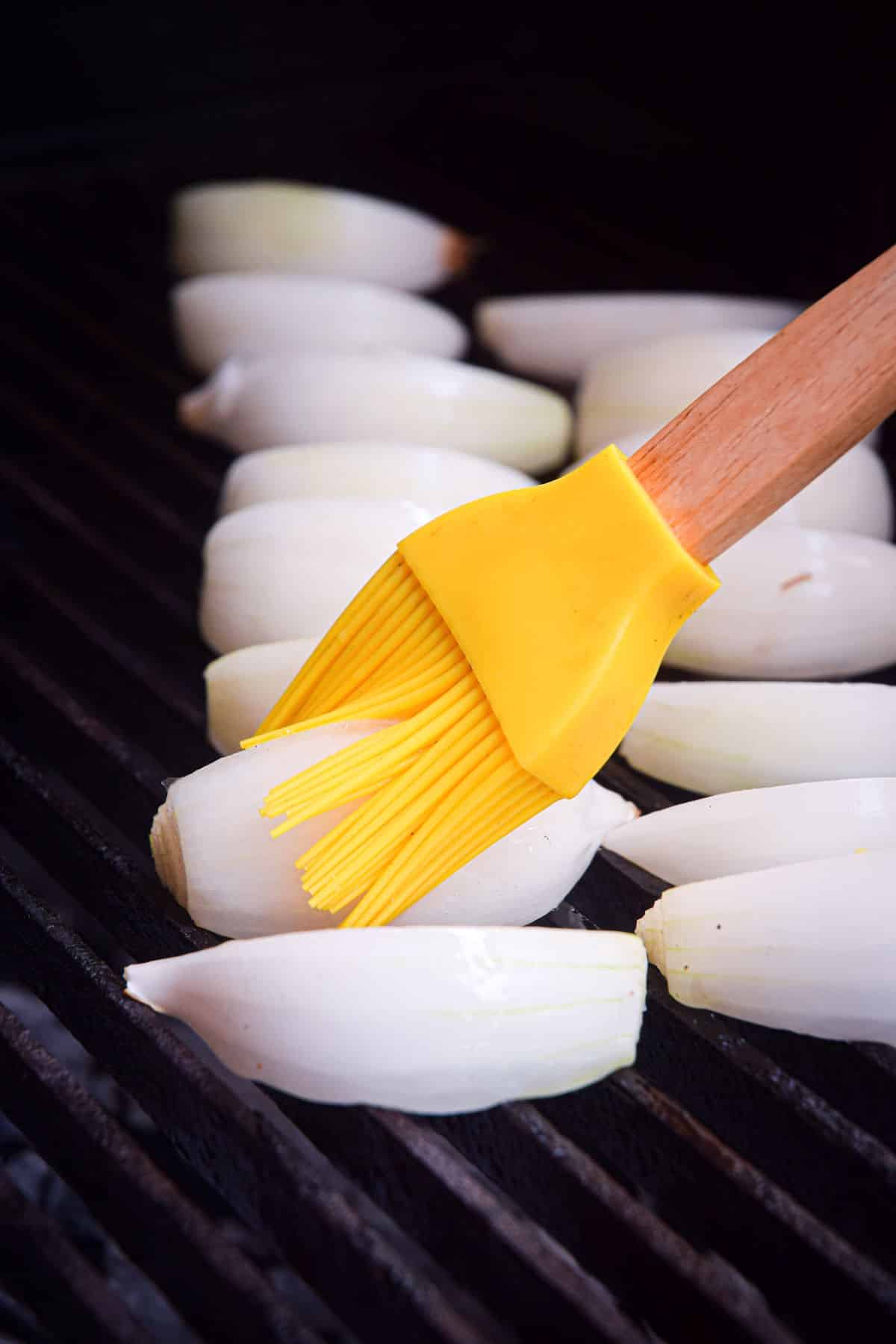 Onion wedges on grill with silicone brush.