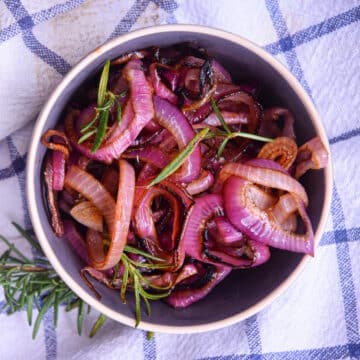 Grilled red onion rings in bowl on kitchen towel.
