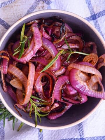 Grilled red onion rings in bowl on kitchen towel.